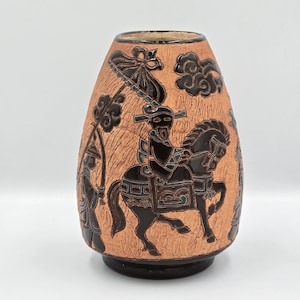 May include: A terracotta vase with a black relief design of figures on horseback and attendants. The vase has a textured surface and a black base, showcasing an Asian-inspired design. The vase is approximately 20 cm tall.