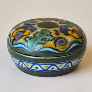 May include: A round ceramic trinket box with a green base and a lid decorated with a colorful floral pattern in shades of blue, yellow, and green.