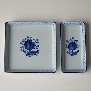 Puede incluir: Dos bandejas de servir de cerámica azul y blanca con un diseño floral. La bandeja más grande es cuadrada y la más pequeña es rectangular.