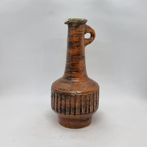 May include: A brown ceramic vase with a green rim and a textured design. The vase has a narrow neck and a wide base.