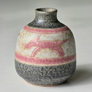 May include: A small, grey ceramic vase with a pink and white design featuring a stylised animal. The vase has a speckled glaze and a rounded shape.
