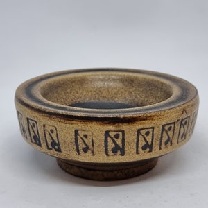 May include: A small, brown ceramic bowl with a black geometric design around the rim. The bowl has a slightly rounded bottom.