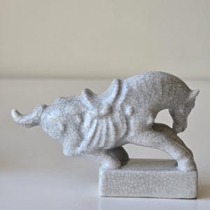 May include: A white ceramic horse figurine with a cracked glaze finish. The horse is in a running pose with its head turned to the side. The figurine is on a square base.