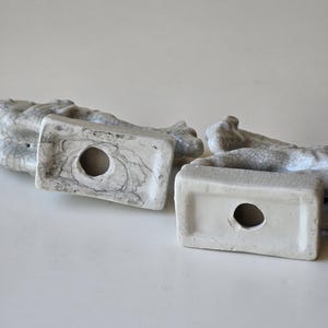 May include: Two white ceramic figurines with a crackled glaze finish. The figurines are in the shape of a seated animal, possibly a dog or cat. The bottom of each figurine has a hole for a candle.