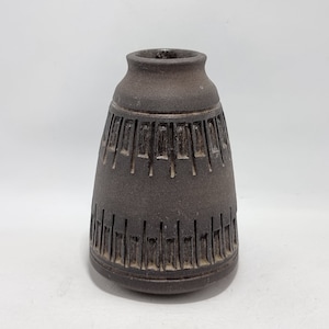 May include: A small, dark brown ceramic vase with a geometric pattern carved into the surface.