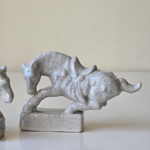 May include: Two gray ceramic horse figurines with a crackled glaze finish. The horses are in a running pose and are on small rectangular bases.