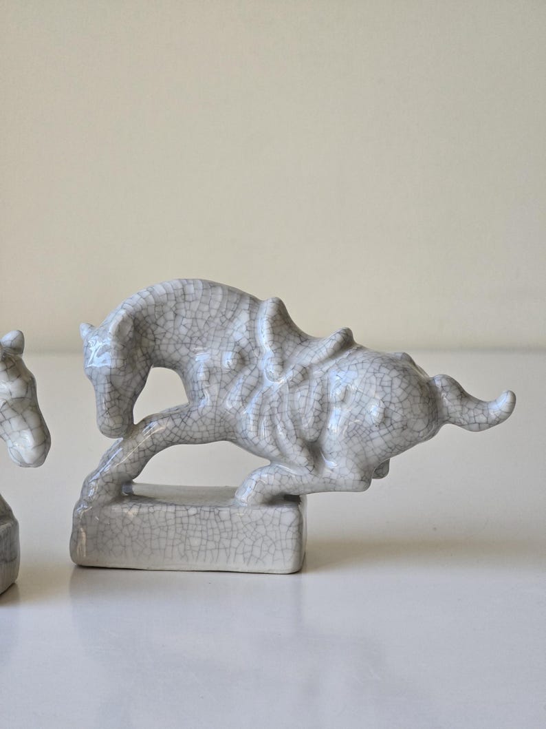 May include: Two gray ceramic horse figurines with a crackled glaze finish. The horses are in a running pose and are on small rectangular bases.