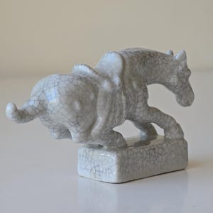 May include: A white ceramic sculpture of a horse and a bull. The sculpture is in a craquelure glaze, which gives it a textured appearance.