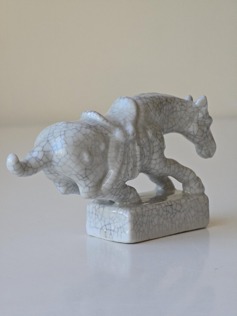 May include: A white ceramic sculpture of a horse and a bull. The sculpture is in a craquelure glaze, which gives it a textured appearance.