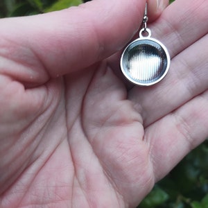 May include: Silver earring with a round, textured pendant. The pendant has a smooth, shiny surface and a slightly raised edge.