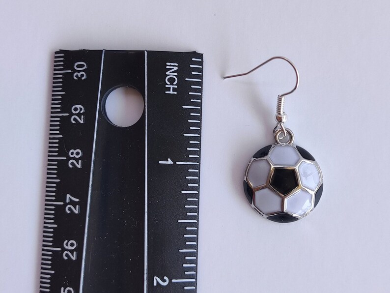 May include: Silver dangle earrings with a black and white soccer ball charm. The soccer ball is about 1 inch in diameter.
