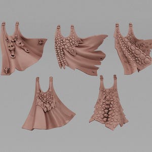 May include: Five miniature, light brown fantasy capes with intricate designs. Each cape features a unique texture, including scales and decorative elements. The capes are displayed against a neutral background, highlighting their detailed craftsmanship.