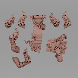 May include: A collection of unpainted light brown miniature gaming components including four flaming skull heads, a vertical scroll with a chain detail, a book held by a gloved hand, and two armored arm segments with flame effects attached to the wrists.