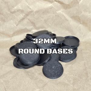 May include: A pile of black circular plastic bases for miniature figures, each measuring 32mm in diameter. The top surface of each base features a textured, gritty finish, while the edges are smooth and raised. The text 32MM ROUND BASES is overlaid.