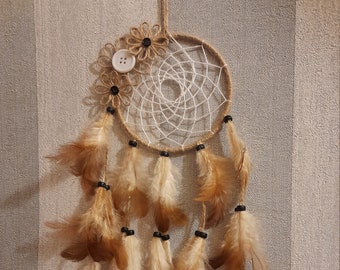 May include: A white and brown dreamcatcher with brown feathers and a white button in the center. The dreamcatcher is decorated with brown twine and small brown flowers.