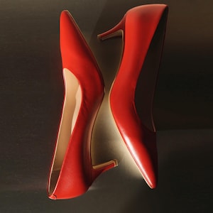 Puede incluir: Un par de zapatos de tacón rojos con punta. Los zapatos tienen un diseño clásico con tacón de aguja. Los zapatos de cuero son de color rojo vibrante y los tacones miden aproximadamente 5 cm de alto.
