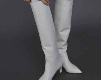 May include: A pair of white leather knee-high boots with a pointed toe and a low block heel.