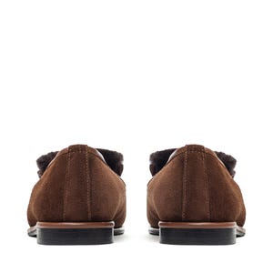 May include: A pair of brown suede loafers with a shearling lining. The shoes have a classic design with a rounded toe and a low heel. The soles are dark brown with a black heel.