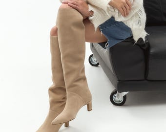 May include: A pair of light brown suede knee-high boots with a pointed toe and a low block heel.