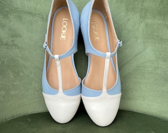 May include: A pair of light blue and white t-strap shoes with the word "LOOKIE" written on the side of each shoe.
