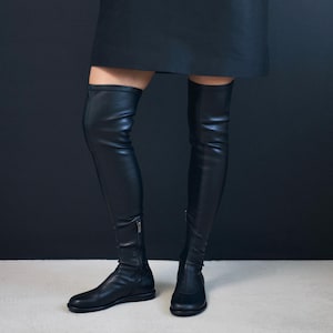 May include: A pair of black over-the-knee boots. The boots are made of a smooth, leather-like material and have a zip detail. The boots extend high up the leg, creating a bold and fashionable look. The boots are a stylish addition to any wardrobe.
