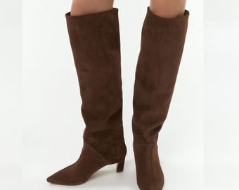 May include: Brown suede knee-high boots with a pointed toe and a low block heel.