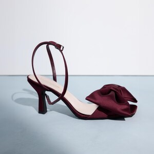 Op de afbeelding: Bordeauxkleurige satijnen sandalen met hak en een grote strik op de teen.