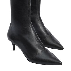 Pu&ograve; includere: Stivali in pelle nera con tacco a stiletto e punta a punta, con gambale elastico.