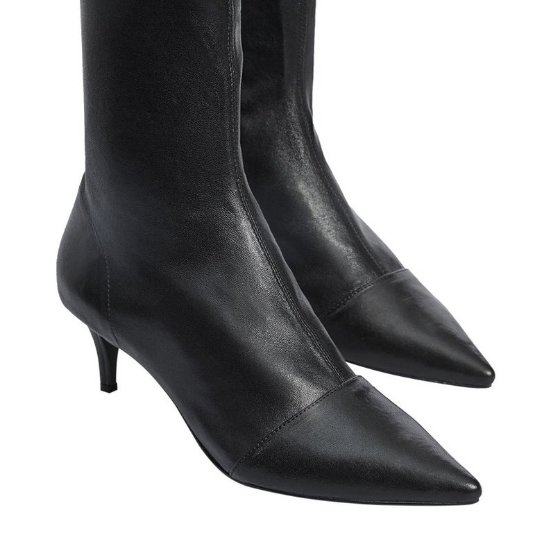 Pu&ograve; includere: Stivali in pelle nera con tacco a stiletto e punta a punta, con gambale elastico.