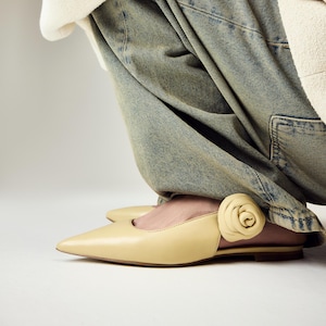Könnte beinhalten: Hellgelbe Leder-Ballerinas mit spitzer Zehenpartie und einer dekorativen Rosenapplikation an der Seite. Die Schuhe stehen vor einem weißen Hintergrund, der ihr Design und ihre Farbe hervorhebt. Ein stilvoller Schuh.