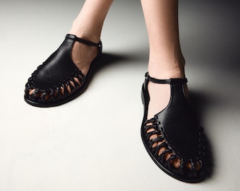 May include: Black leather sandals with a woven design and an ankle strap.