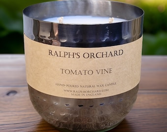 May include: A silver-colored candle in a hammered metal container. The candle has two wicks and a label that reads "RALPH'S ORCHARD TOMATO VINE." The candle is hand-poured and made in England.