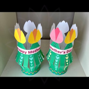 May include: Two green paper flower pots with yellow and pink flowers. One pot says "Happy Mother" and the other says "Mother's Day".