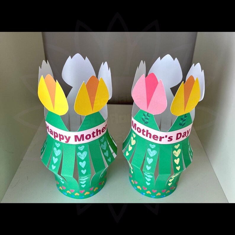 May include: Two green paper flower pots with yellow and pink flowers. One pot says "Happy Mother" and the other says "Mother's Day".