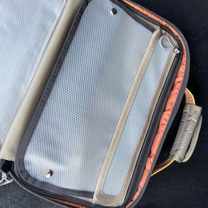 May include: A black travel bag with a zippered compartment and a mesh pocket. The bag has a brown trim and a gray handle.