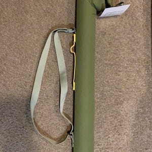 May include: Olive green fishing rod case with a black base and a matching shoulder strap. The case has a zippered top with a gold graphic of a fishing lure. A white tag is attached to the top.