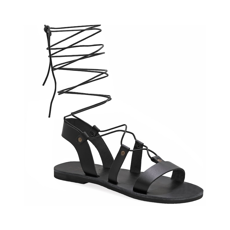 May include: Black leather sandals with lace-up ties that wrap around the ankle. The sandals have a flat sole and a simple design.