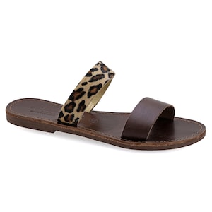 May include: Brown leather sandals with a leopard print strap. The sandals have a flat sole and two straps, one across the toes and the other across the top of the foot. The sandals are made in Greece.