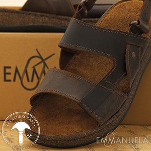 May include: Brown leather sandals with multiple straps and a cork footbed. The sandals have adjustable buckles and are designed for comfort. The image also shows the brand name "Emmanuela" and the words "Leathercraft" and "Finest Quality".