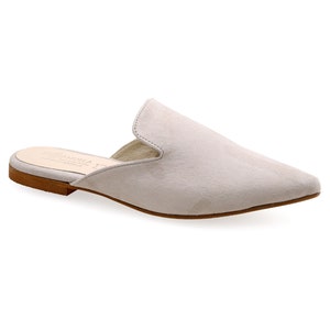 May include: A light gray suede mule shoe with a pointed toe. The shoe has a low heel and a slip-on design. The sole is a light brown color. The shoe is a neutral color and can be worn with many outfits.