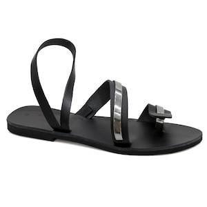 May include: Black leather sandals with a silver strap detail. The sandals have a toe loop and an ankle strap.