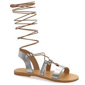 May include: Silver leather sandals with brown laces that wrap up the leg. The sandals have a flat sole and a simple design.