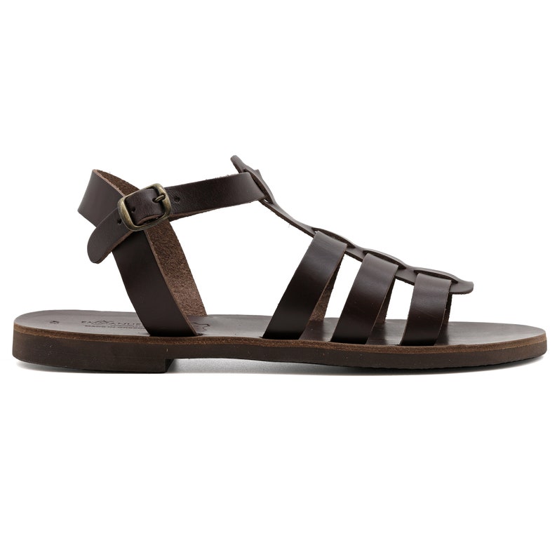 May include: Brown leather sandals with a cage-like design. The sandals feature a T-strap and an ankle strap with a buckle. The sole is flat and the leather has a natural, textured appearance. A classic, open-toe footwear.