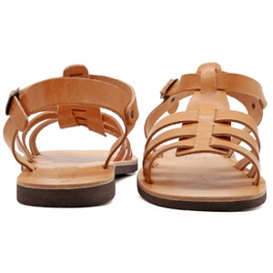 May include: A pair of tan leather sandals with multiple straps and buckles. The sandals have a dark brown sole and a classic gladiator style. The footwear is designed for comfort and style, suitable for warm weather.