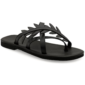 May include: Black leather sandals with a leaf-like design across the top. The sandals have a toe loop and multiple straps. The sole is flat and black. These sandals are suitable for casual wear.