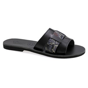 Op de afbeelding: Zwarte leren slippers met een slangenvormig bandje over de bovenkant. De slippers hebben een platte zool en een eenvoudig ontwerp.