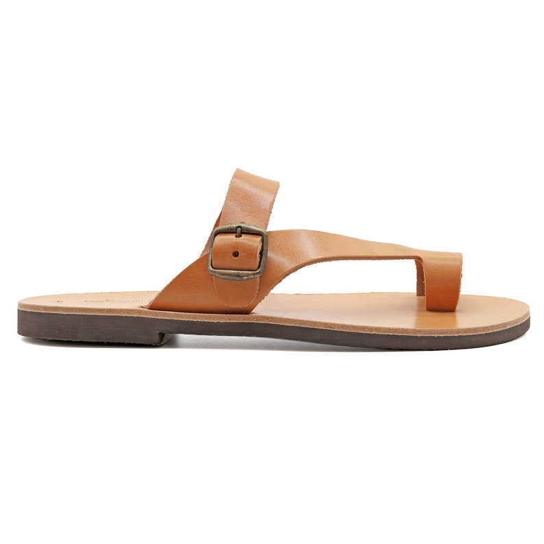 May include: Tan leather sandals with a buckle strap and a toe loop. The sandals have a brown leather sole.