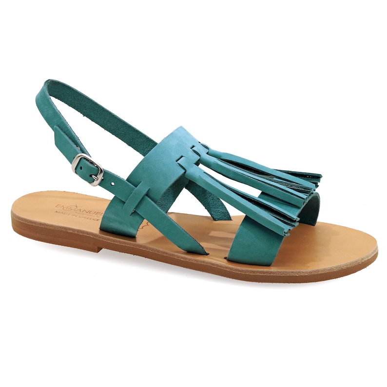 May include: Teal leather sandals with a flat sole and an ankle strap with a buckle. The sandals have a decorative fringe detail across the top. The footbed is light tan. Made in Greece.