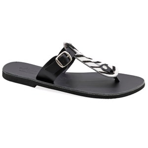 May include: Black leather sandals with a zebra print strap and a buckle closure. The sandals are made in Greece.