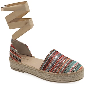 May include: Espadrille sandal with a woven upper in shades of red, orange, and teal, with a beige ankle wrap. The sole is made of woven jute. The sandal has a small wedge heel.